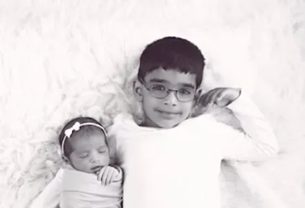 Big brother posing gently with his newborn sister
