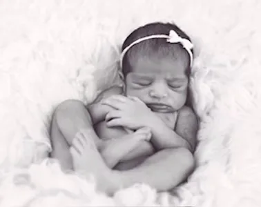 Newborn with a bow headband sleeping with arms crossed